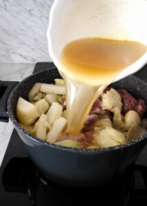 adding vegetable stock to lamb artichoke pot